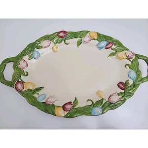 May include: Oval serving platter with a cream-colored center and green handles. The rim is decorated with a garland of colorful tulips in shades of red, yellow, pink, and blue. A decorative piece for serving food.