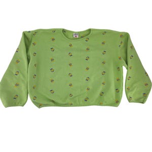 May include: A light green sweatshirt with a crew neck and long sleeves. The sweatshirt is covered in a pattern of yellow and blue cartoon-like designs. The brand name "LIME" is visible on a small tag near the neckline. The bottom hem is elasticized.