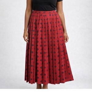 May include: A red pleated skirt with a repeating navy blue geometric pattern. The skirt is knee-length and has a high waist. The fabric appears to be a medium-weight material.