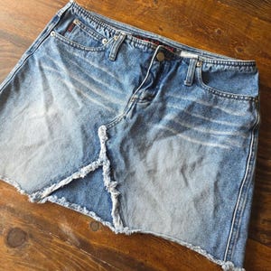 Op de afbeelding: Een lichtblauwe spijkerbroekrok met een gerafelde zoom en een split aan de voorkant. De rok heeft een klassiek ontwerp met vijf zakken met een knoop- en ritssluiting. De denim heeft een vervaagd waseffect.
