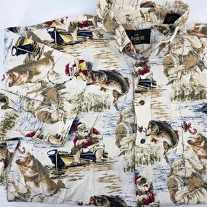 Puede incluir: Camisa abotonada de color crema con un estampado repetido de Papá Noel pescando y peces grandes. La camisa tiene cuello y mangas largas. La marca "RedHead" es visible en una etiqueta.