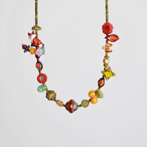 Op de afbeelding: Een kleurrijke ketting met kralen met een vossenbedel, bloemen en verschillende gevormde kralen. De ketting bevat rode, oranje, gele en groene kralen. De ketting is geregen op een groen koord.