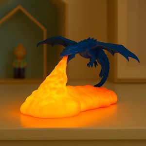 May include: A blue dragon figurine with outstretched wings, exhaling a stream of orange light. The light forms a cloud-like shape. The dragon is a fantasy-themed decorative item.