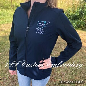 May include: A navy blue softshell jacket with a white embroidered heart containing the letters "RN" and a stethoscope. The name "Nikki" is embroidered below the heart.