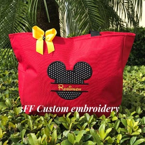 Peut inclure: Sac fourre-tout rouge avec une t&ecirc;te de Mickey Mouse brod&eacute;e en noir et blanc &agrave; pois blancs. Le nom "Robinson" est brod&eacute; en jaune sous la t&ecirc;te de Mickey Mouse. Le texte "3FF Custom embroidery" est imprim&eacute; en jaune au bas du sac.