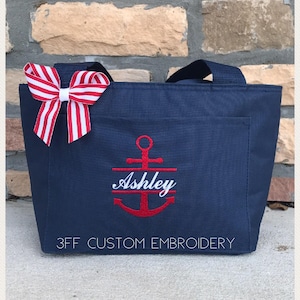 May include: A navy blue tote bag with a red anchor and the name "Ashley" embroidered on it. The bag has a red and white striped bow on the handle. The text "3FF CUSTOM EMBROIDERY" is printed on the bottom of the bag.