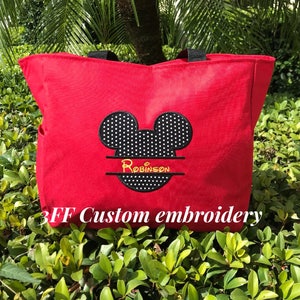 Peut inclure: Sac fourre-tout en toile rouge avec des oreilles de Mickey Mouse &agrave; pois noirs et blancs et le nom "Robinson" brod&eacute; en jaune. Le sac a des anses noires et le texte "3FF Custom embroidery" est imprim&eacute; en bas.