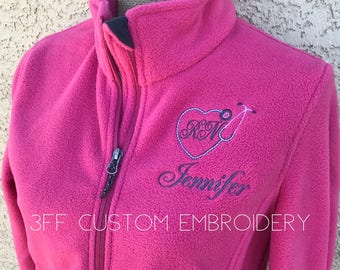 May include: A pink fleece jacket with a heart and stethoscope embroidered on the front. The text "Jennifer" is embroidered below the heart. The text "3FF CUSTOM EMBROIDERY" is printed on the bottom of the jacket.