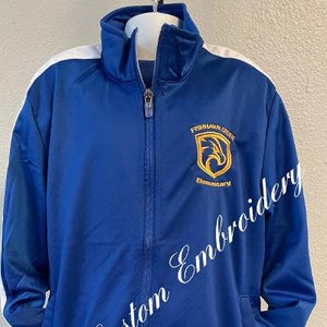 May include: A blue and white zippered jacket with a white stripe down each sleeve. The jacket has a gold embroidered logo that says "Fishhawk Creek Elementary".