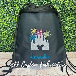May include: Black drawstring bag with an embroidered design of a silver castle with fireworks and a Mickey Mouse head. The bag also has the name "Lorraine" embroidered on it. The text "3FF Custom Embroidery" is visible at the bottom of the bag.