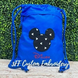 May include: A blue drawstring bag with a black and white Mickey Mouse head embroidered on the front. The bag also has the text "Dillon" and "3FF Custom Embroidery" embroidered on it.