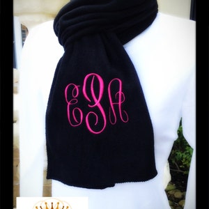 May include: Black fleece scarf with a pink monogram "EGA" embroidered on it.