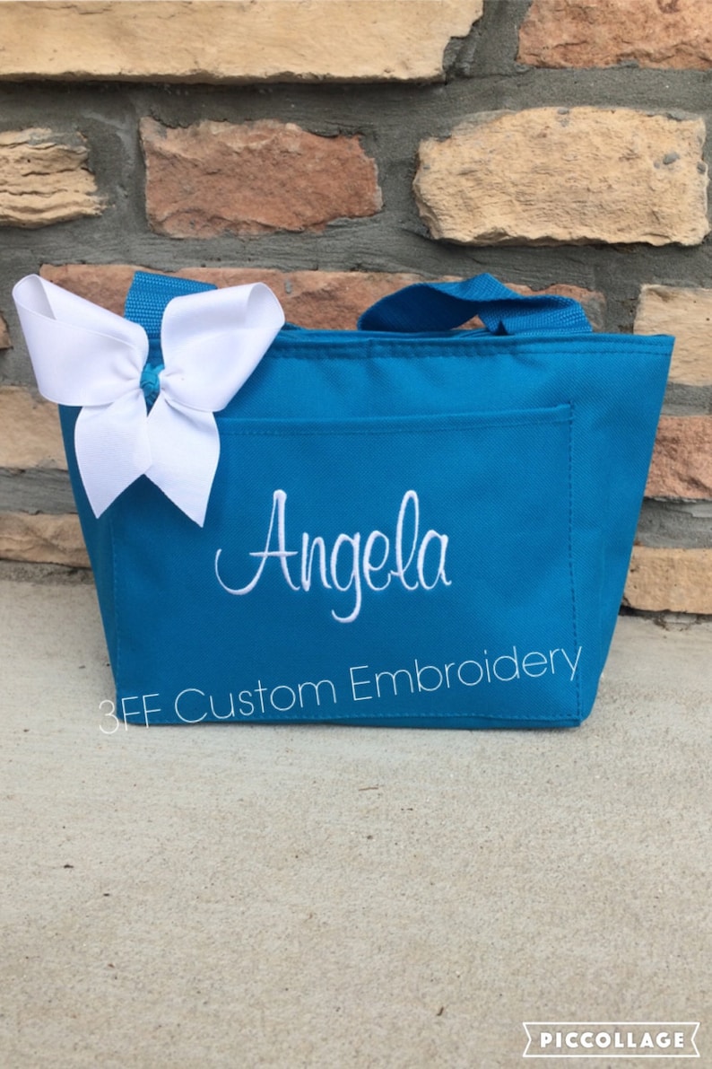 May include: A turquoise tote bag with a white bow on top and the name "Angela" embroidered on the front. The bag also has the text "3FF Custom Embroidery" on the front.