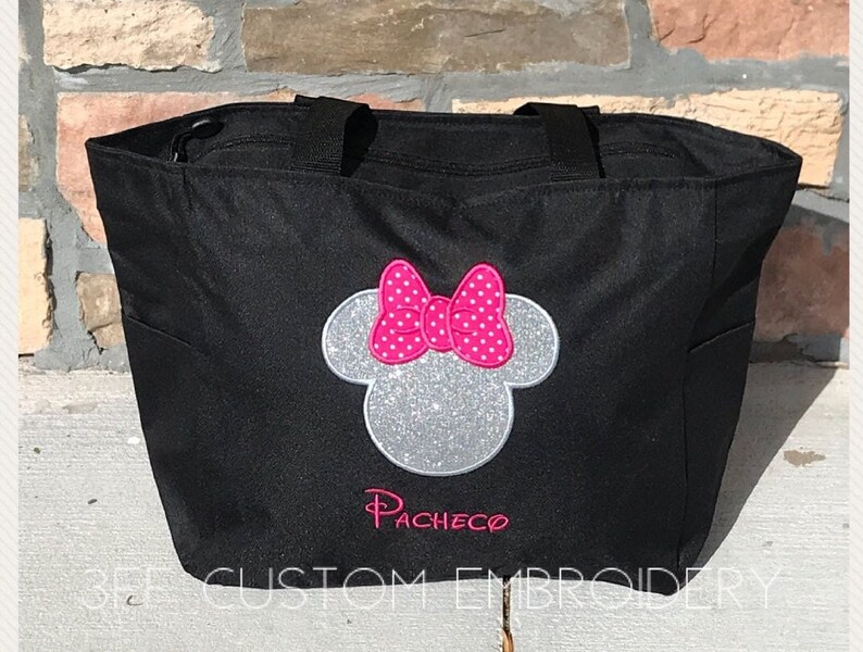 May include: Black tote bag with a silver glitter Minnie Mouse head with a pink polka dot bow and the name "Pacheco" embroidered in pink.