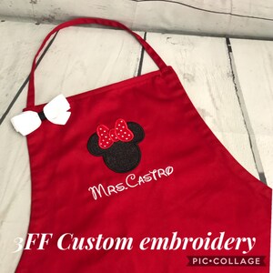 May include: Red apron with a white bow and embroidered Minnie Mouse head with the text "Mrs. Castro" in white thread.