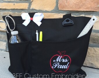 May include: Black tote bag with multiple pockets and a red apple with white embroidery that says "Mrs. Paul".