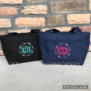Puede incluir: Dos bolsas de almuerzo aisladas con monogramas personalizados. La bolsa de la izquierda es negra con un monograma turquesa y la bolsa de la derecha es azul marino con un monograma rosa. Ambas bolsas tienen un dise&ntilde;o de flechas blancas alrededor del monograma.