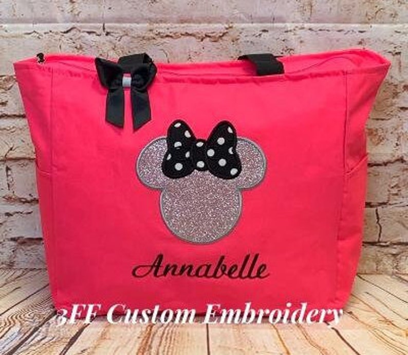 May include: A bright pink tote bag with black straps and a black and white polka dot Minnie Mouse design. The bag is personalized with the name "Annabelle" and the text "3FF Custom Embroidery".