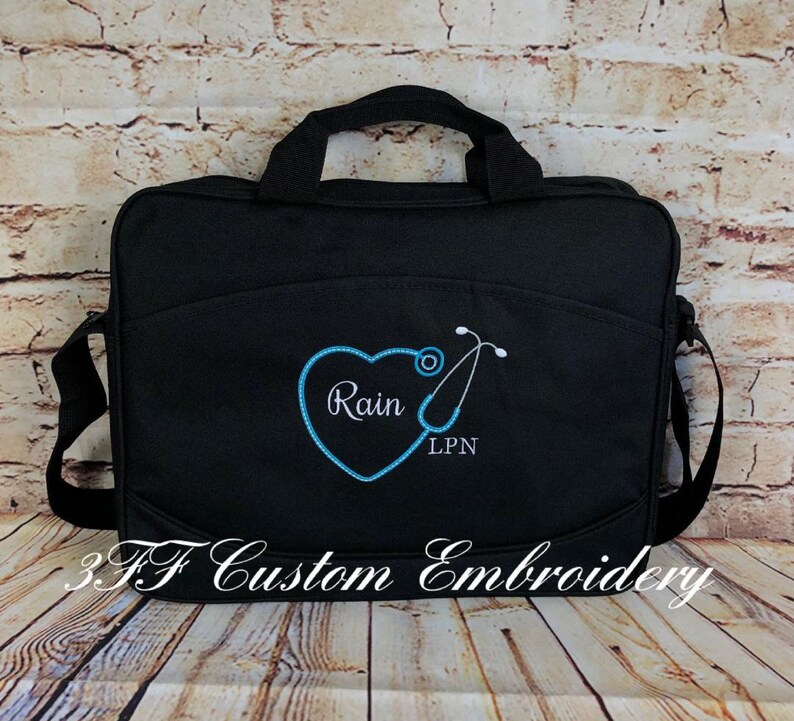 May include: Black canvas messenger bag with a blue embroidered heart and stethoscope. The heart has the name "Rain" and the text "LPN" embroidered inside.