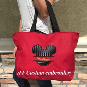 Peut inclure: Sac fourre-tout en toile rouge avec des anses noires et une t&ecirc;te de Mickey Mouse noire et blanche avec le nom "Robinson" brod&eacute; en jaune. Le sac porte l'inscription "3FF Custom embroidery" imprim&eacute;e sur le devant.