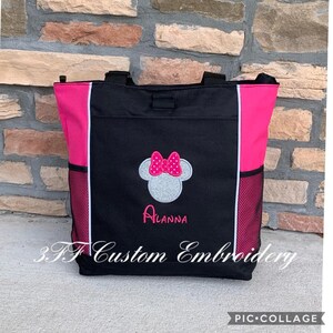 May include: Black tote bag with pink accents and a white mesh pocket. The bag features an embroidered Minnie Mouse head with a pink bow and the name "Alanna" underneath. The bag is made by 3F Custom Embroidery.