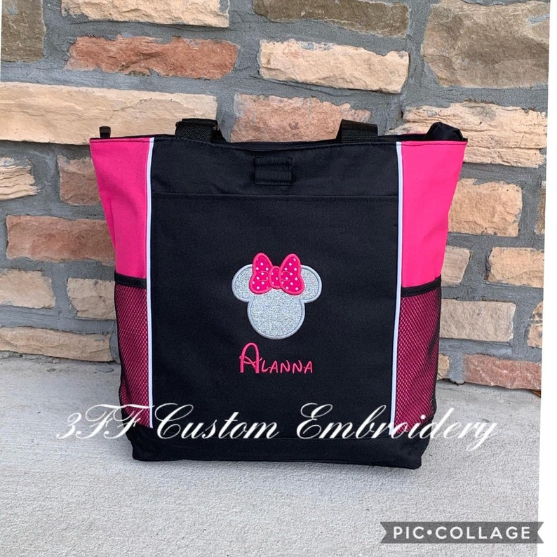 May include: Black tote bag with pink accents and a white mesh pocket. The bag features an embroidered Minnie Mouse head with a pink bow and the name "Alanna" underneath. The bag is made by 3F Custom Embroidery.
