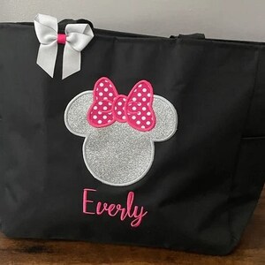 May include: Black tote bag with a silver glitter Minnie Mouse head and pink bow with white polka dots. The name "Everly" is embroidered in pink below the Minnie Mouse head.