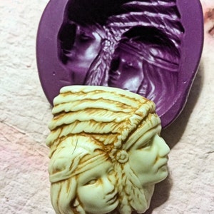 Op de afbeelding: Een paar Native American-geïnspireerde figuren met hoofdtooien, gebeeldhouwd in een lichtbruine kleur. De figuren bevinden zich in een siliconenmal, die paars is.