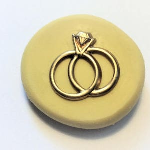 May include: A silicone mould for making cake decorations, featuring a design of two gold rings with a diamond.