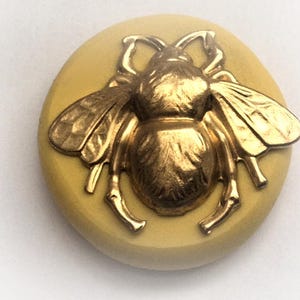 May include: A gold bee button with a yellow background. The bee is detailed with raised wings and legs.