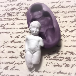 Puede incluir: Una figurita de cerámica blanca de un niño con un molde de silicona morado. La figurita le falta un brazo y tiene una cara detallada.