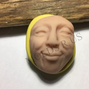 Peut inclure: Un moule en silicone jaune en forme de visage souriant avec les yeux fermés. Le moule est destiné à la fabrication de décorations de gâteaux ou d'autres objets artisanaux.