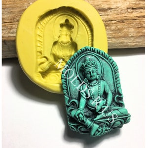 May include: A silicone mold for making a small, detailed figurine of a seated Buddha. The mold is yellow and the figurine is green.