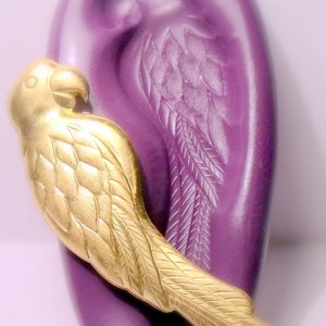 May include: A gold-coloured parrot figurine with detailed feathers, perched on a purple ear-shaped base.