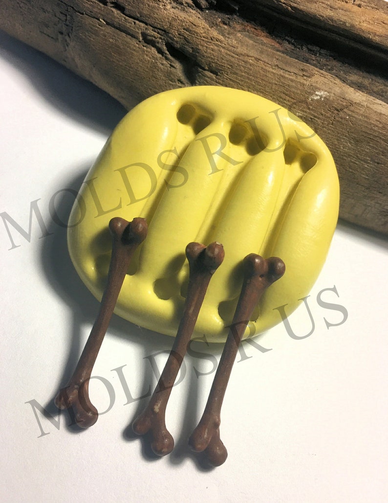 May include: A yellow silicone mold with three bone-shaped cavities. Three brown bone-shaped candies are shown next to the mold.