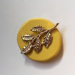 May include: A gold-colored metal leaf branch design on a yellow round silicone mold.
