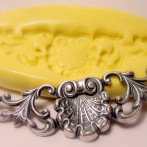 Könnte beinhalten: Eine gelbe Silikonform mit einem detaillierten Design einer dekorativen Rolle mit einer Muschel in der Mitte. Die Form wird verwendet, um Kuchendekorationen oder andere essbare Handwerke herzustellen.