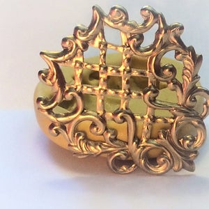 May include: A gold-colored metal mold for making decorative cake toppers or other crafts. The mold features a detailed design with a grid pattern and intricate scrollwork.