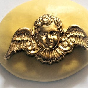 May include: A gold cherub with wings, set against a yellow oval background.