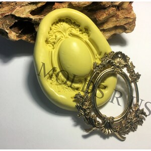 Puede incluir: Un molde de silicona para hacer un marco ovalado decorativo. El molde es amarillo y tiene un diseño detallado. Un marco de metal dorado se muestra al lado del molde.