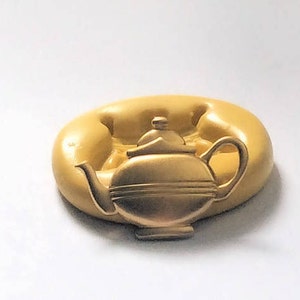 Könnte beinhalten: Eine goldfarbene Teekannenform aus Silikon für die Herstellung von Kuchendekorationen. Die Form ist detailliert gestaltet.