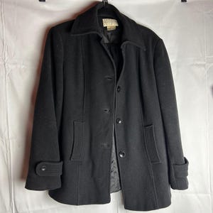 May include: A black wool coat with a notched collar, button closure, and front pockets. The coat has long sleeves with buttoned cuffs. The coat is hanging on a black hanger against a white background.