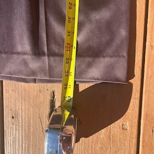 K&ouml;nnte beinhalten: Nahaufnahme einer dunkelvioletten Hose mit einem Ma&szlig;band, das eine L&auml;nge von etwa 91 cm anzeigt. Die Hose ist aus einem glatten Stoff gefertigt und ist teilweise gefaltet. Das Ma&szlig;band ist gelb mit schwarzen Markierungen.