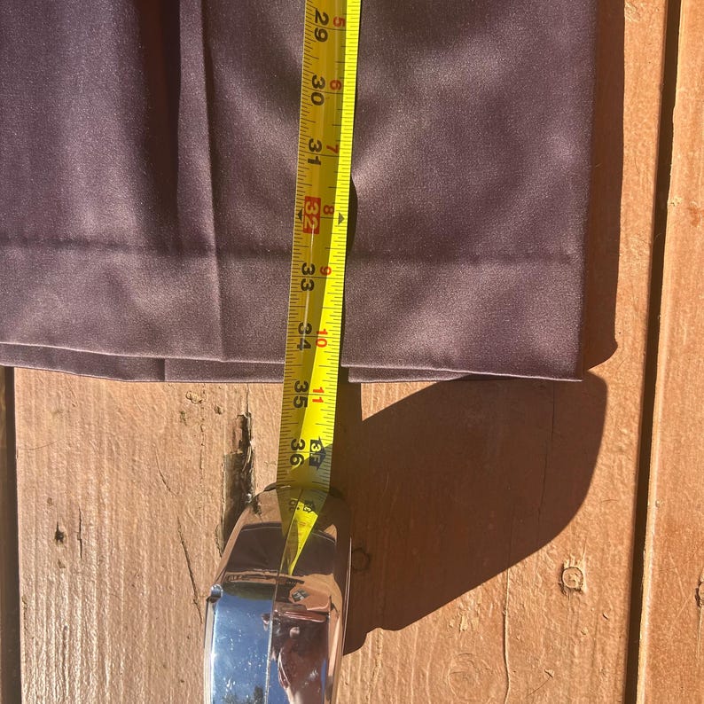 K&ouml;nnte beinhalten: Nahaufnahme einer dunkelvioletten Hose mit einem Ma&szlig;band, das eine L&auml;nge von etwa 91 cm anzeigt. Die Hose ist aus einem glatten Stoff gefertigt und ist teilweise gefaltet. Das Ma&szlig;band ist gelb mit schwarzen Markierungen.