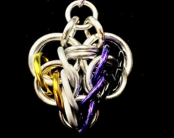 Könnte beinhalten: Handgefertigter Kettenanhänger mit dem Design der nicht-binären Pride-Flagge. Der Anhänger besteht aus silberfarbenen Metallringen mit Akzenten aus goldenen, weißen, lila und schwarzen Ringen. Er hängt an einem lila-weißen Band vor schwarzem Hintergrund.