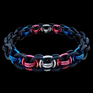 Könnte beinhalten: Ein schwarzes Kettenarmband mit blauen, rosa und silbernen Akzenten. Das Armband besteht aus ineinandergreifenden Ringen, wobei die blauen und rosa Ringe in das Design eingestreut sind. Der Hintergrund ist schwarz.