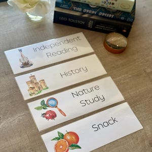 Könnte beinhalten: Vier weiße rechteckige Etiketten mit Text und Illustrationen für Unabhängiges Lesen, Geschichte, Naturstudium und Snack. Ein Stapel Bücher und eine Lupe sind ebenfalls sichtbar.