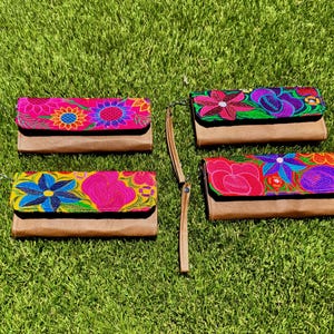 Può includere: Quattro pochette ricamate con motivi floreali. Ogni pochette presenta una base in pelle marrone e una parte superiore ricamata vibrante con fiori nei toni del rosa, blu, viola e giallo. Le pochette hanno cinturini da polso.