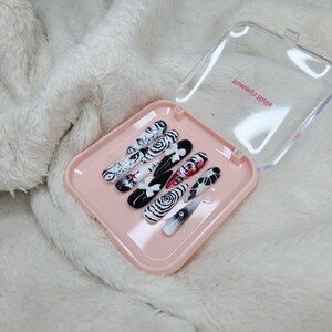 May include: A set of press-on nails in a pink case. The nails feature various black and white designs, including swirls, floral patterns, and abstract art. Some nails have red accents. The case has the text "Homemade Nails".