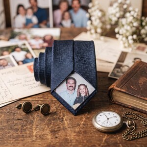 May include: A dark navy blue necktie featuring a textured fabric finish and a custom rectangular photo print on the front blade. The photograph displays a man and a young girl. The tie is accompanied by two round metal cufflinks and a pocket watch.